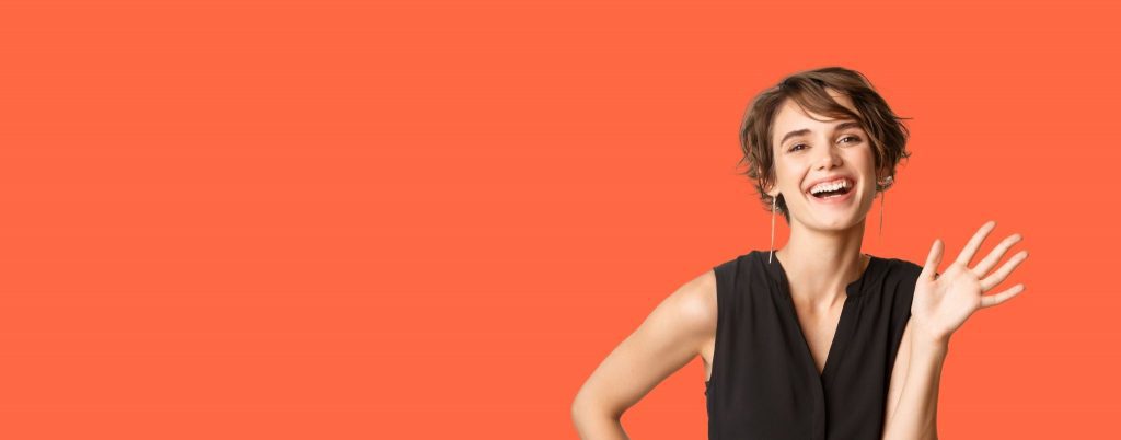 Lady on orange background wearing a black dress saying hello with a cheerful smile